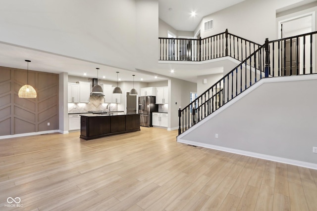 unfurnished living room with sink, light hardwood / wood-style flooring, and a high ceiling