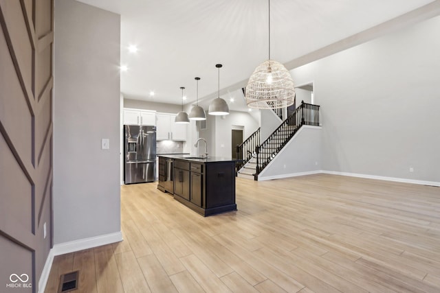 kitchen featuring decorative light fixtures, appliances with stainless steel finishes, white cabinets, a kitchen island with sink, and backsplash