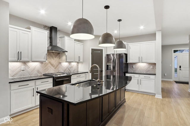 kitchen with wall chimney exhaust hood, sink, hanging light fixtures, appliances with stainless steel finishes, and a kitchen island with sink