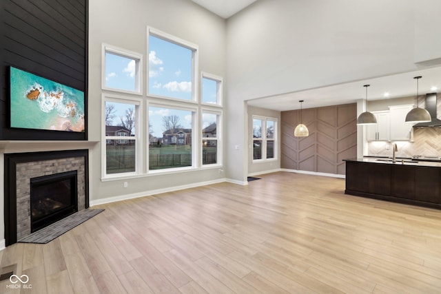 unfurnished living room featuring a towering ceiling, sink, a fireplace, and light wood-type flooring