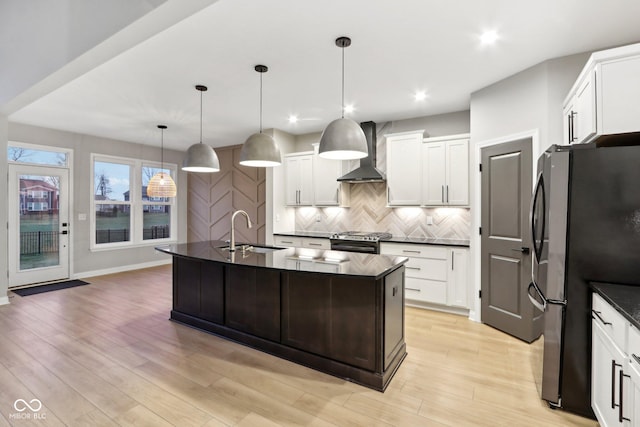 kitchen featuring appliances with stainless steel finishes, decorative light fixtures, sink, a kitchen island with sink, and wall chimney range hood