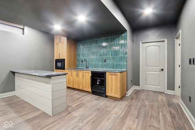 bar featuring black microwave, sink, beverage cooler, and light wood-type flooring