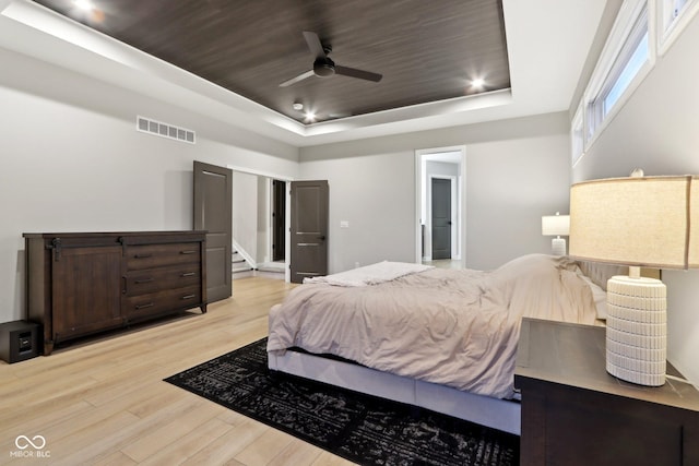 bedroom with ceiling fan, light wood-type flooring, wood ceiling, and a tray ceiling