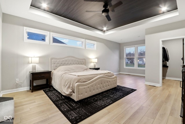 bedroom with a raised ceiling, light wood-type flooring, ceiling fan, and multiple windows