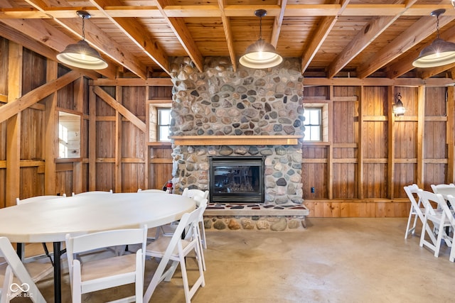 dining area with beamed ceiling, wood walls, concrete floors, a fireplace, and wood ceiling