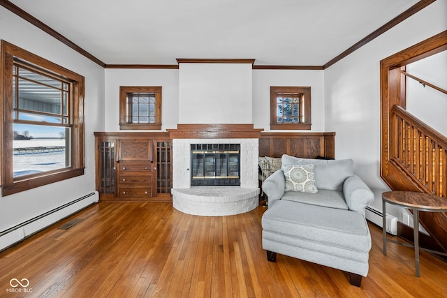 living room with hardwood / wood-style floors, a baseboard radiator, a brick fireplace, and ornamental molding