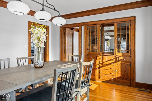 dining space with ornamental molding and light hardwood / wood-style flooring