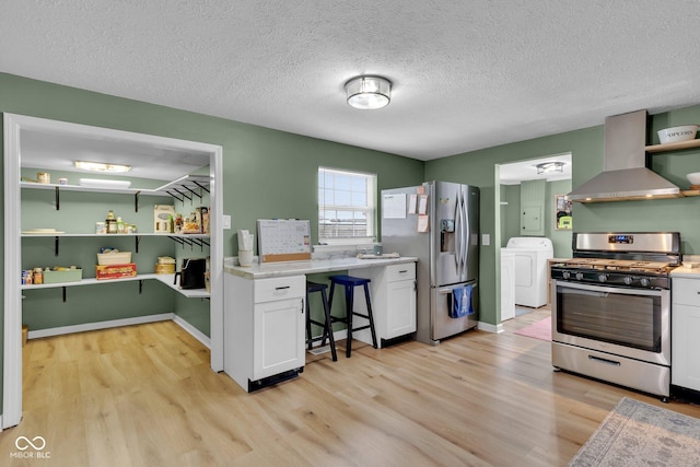 kitchen with white cabinetry, light wood-style floors, appliances with stainless steel finishes, wall chimney exhaust hood, and washer / clothes dryer