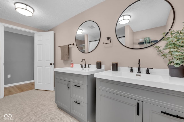 full bath with a sink, a textured ceiling, and two vanities