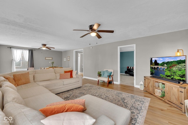 living room featuring baseboards, ceiling fan, a textured ceiling, and light wood-style floors