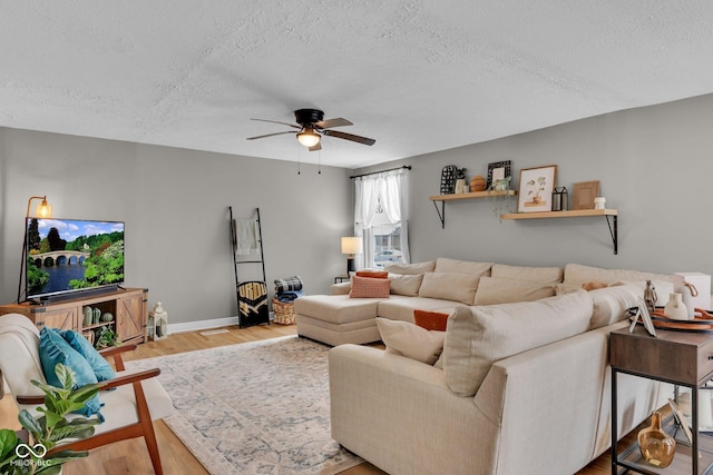 living room with light wood-type flooring, ceiling fan, and a textured ceiling