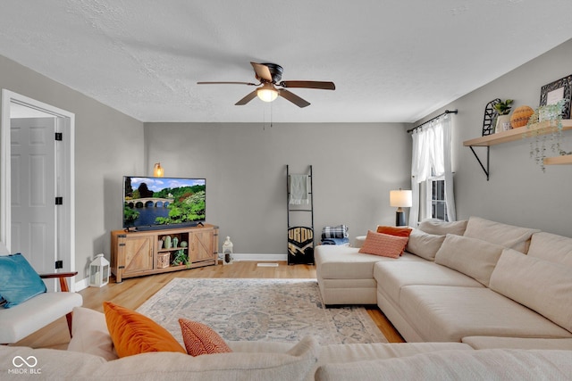 living room with ceiling fan, light wood-style flooring, baseboards, and a textured ceiling