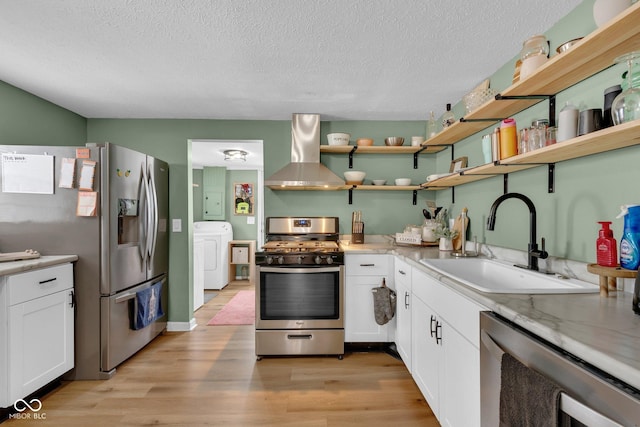 kitchen with light wood-style flooring, appliances with stainless steel finishes, a sink, wall chimney range hood, and washer / dryer