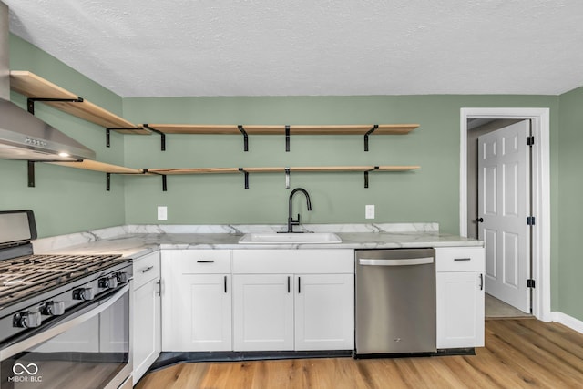 kitchen featuring wall chimney exhaust hood, appliances with stainless steel finishes, light stone countertops, open shelves, and a sink