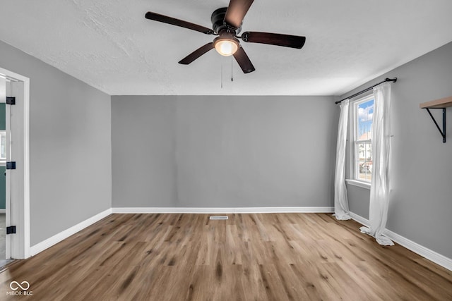 spare room with a textured ceiling, wood finished floors, visible vents, and baseboards