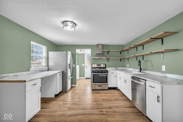 kitchen with light wood finished floors, open shelves, appliances with stainless steel finishes, a sink, and wall chimney exhaust hood