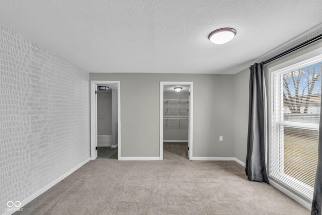 unfurnished bedroom featuring a textured ceiling, brick wall, carpet, and a walk in closet