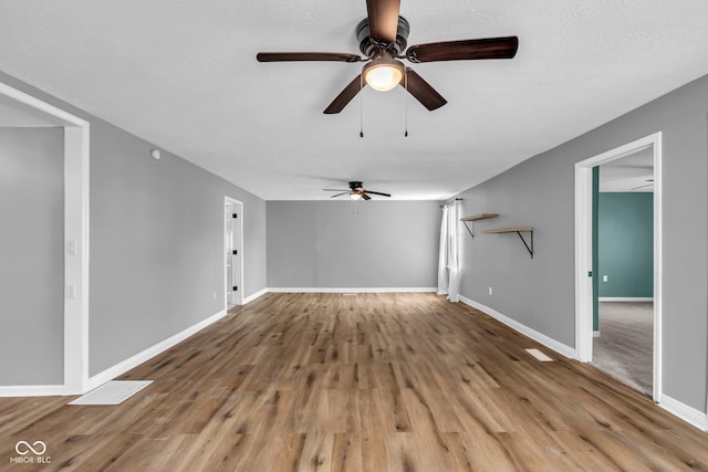 unfurnished living room featuring ceiling fan, a textured ceiling, baseboards, and wood finished floors