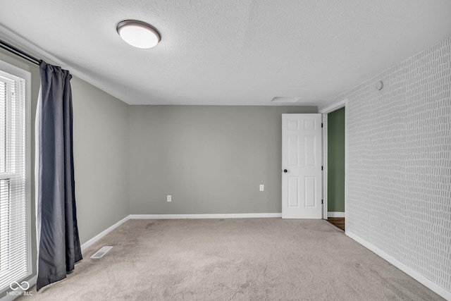 carpeted spare room with baseboards, brick wall, visible vents, and a textured ceiling