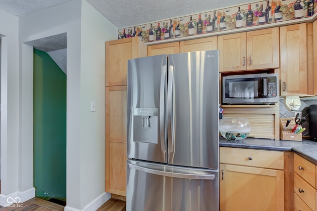 kitchen with light brown cabinets, a textured ceiling, stainless steel appliances, and hardwood / wood-style flooring