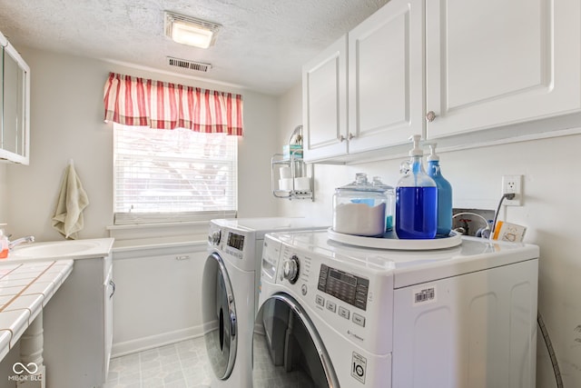 clothes washing area featuring washer and dryer, cabinets, and a textured ceiling