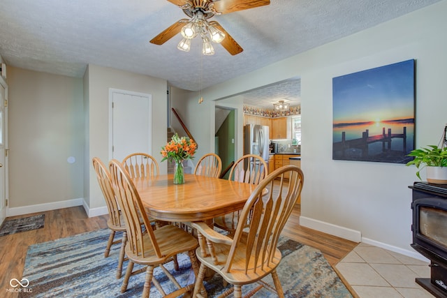 dining area with a wood stove, ceiling fan, light hardwood / wood-style floors, and a textured ceiling