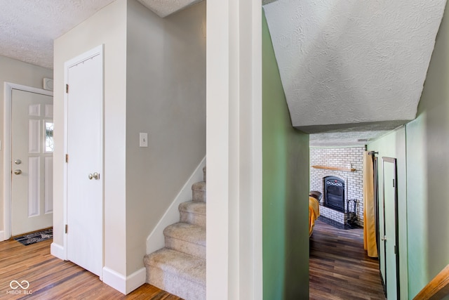 staircase featuring a wood stove, wood-type flooring, and a textured ceiling