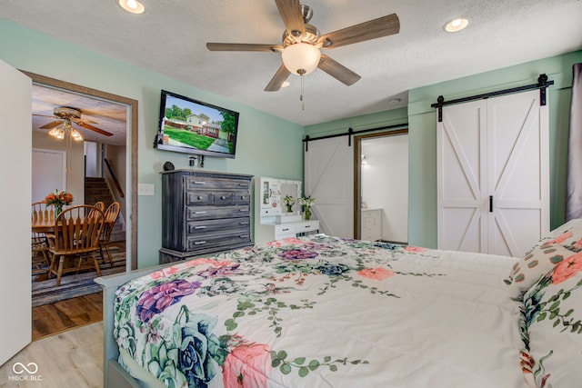 bedroom with a barn door, ceiling fan, a textured ceiling, and light wood-type flooring