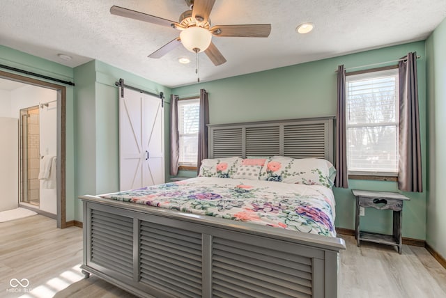 bedroom featuring light wood-type flooring, a barn door, multiple windows, and ceiling fan