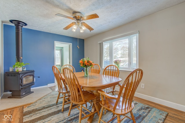 dining area with a wood stove, ceiling fan, light hardwood / wood-style flooring, and a textured ceiling