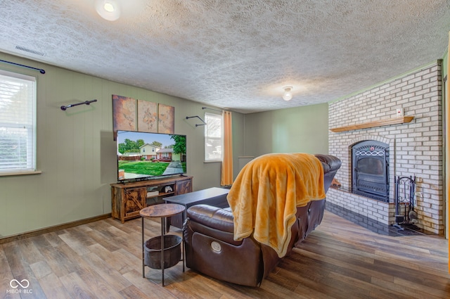 living room with wood-type flooring, a textured ceiling, and a brick fireplace