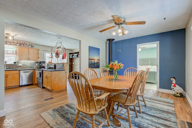 dining area featuring a textured ceiling, light hardwood / wood-style floors, a wood stove, and ceiling fan