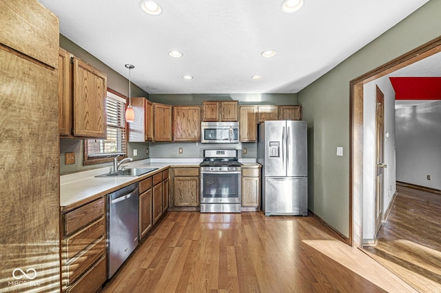 kitchen featuring decorative light fixtures, sink, stainless steel appliances, and light hardwood / wood-style flooring