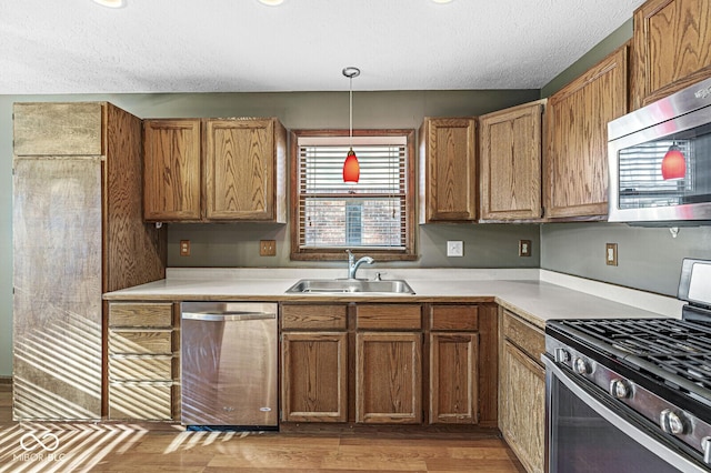 kitchen with sink, pendant lighting, a textured ceiling, and appliances with stainless steel finishes