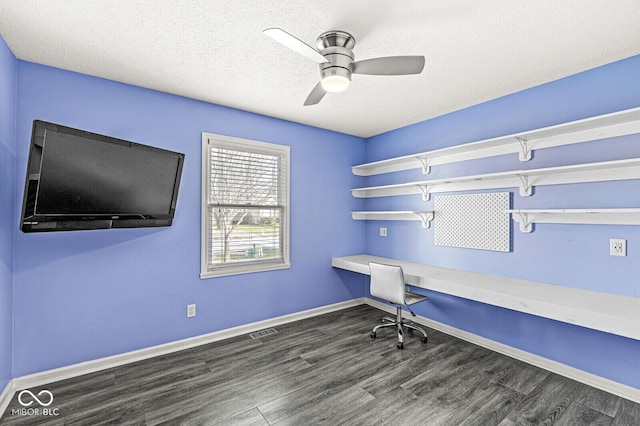 unfurnished office with ceiling fan, dark hardwood / wood-style flooring, built in desk, and a textured ceiling