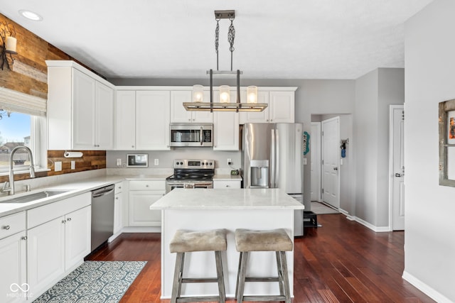 kitchen with sink, white cabinetry, decorative light fixtures, appliances with stainless steel finishes, and a kitchen island