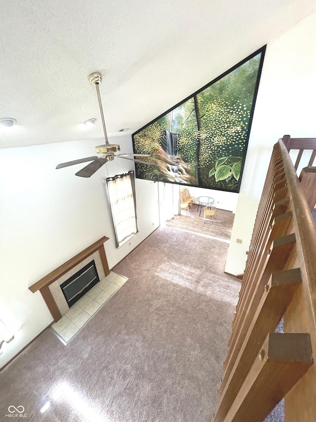 unfurnished living room with a tiled fireplace, ceiling fan, light carpet, and a textured ceiling