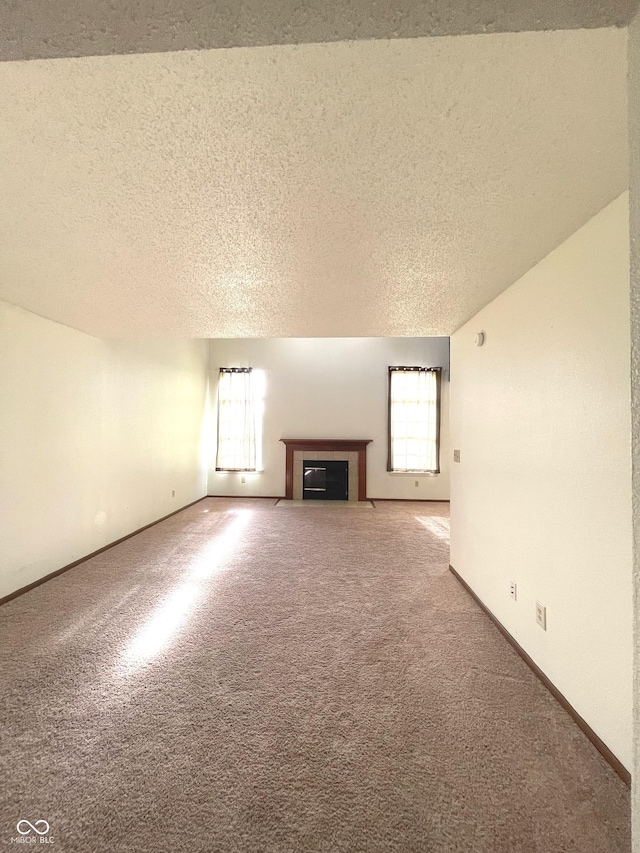 unfurnished living room featuring a tiled fireplace, carpet, and a textured ceiling