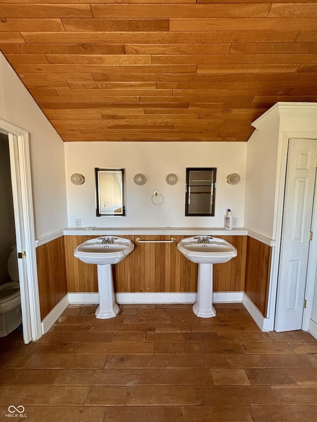 bathroom featuring wooden ceiling, toilet, wood finished floors, vaulted ceiling, and wainscoting