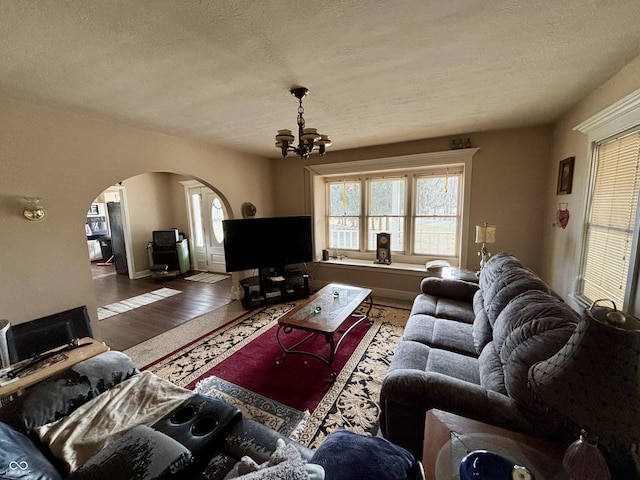 living area with a chandelier, arched walkways, plenty of natural light, and wood finished floors