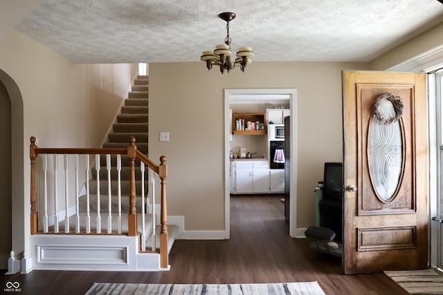 foyer entrance featuring arched walkways, an inviting chandelier, dark wood-type flooring, a textured ceiling, and baseboards