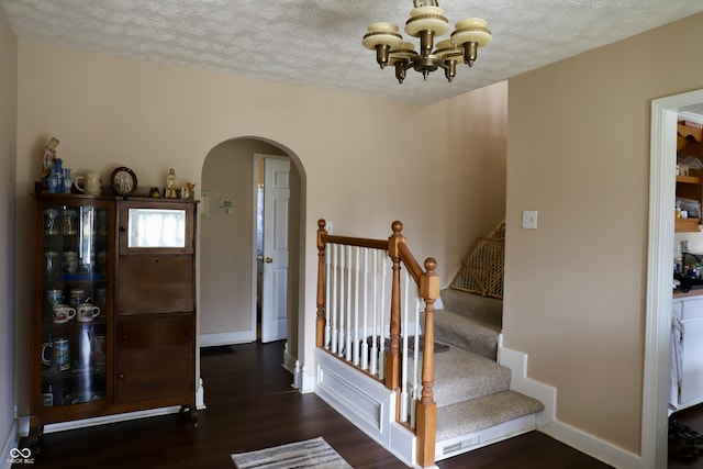 entrance foyer with arched walkways, a textured ceiling, baseboards, and wood finished floors