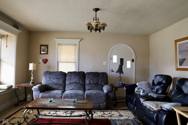 living room featuring a chandelier, arched walkways, light colored carpet, and baseboards