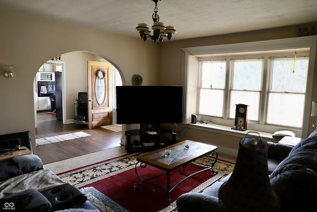 living area featuring arched walkways, baseboards, wood finished floors, and an inviting chandelier