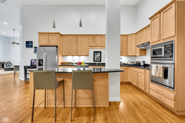 kitchen featuring a high ceiling, light hardwood / wood-style flooring, appliances with stainless steel finishes, a kitchen island, and a kitchen bar