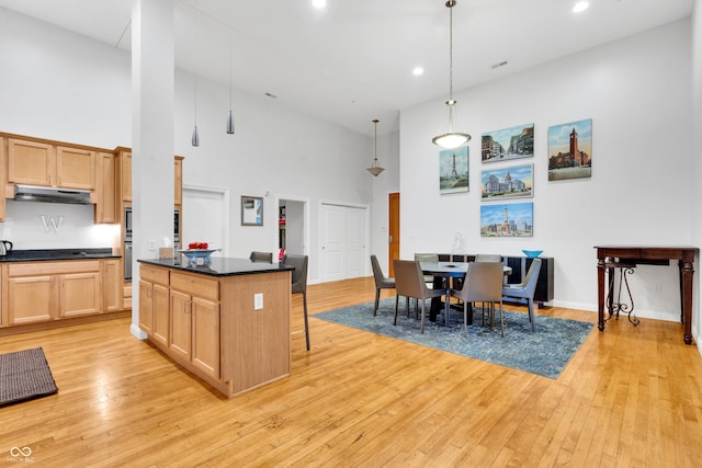 kitchen featuring a kitchen bar, light brown cabinets, a towering ceiling, and decorative light fixtures