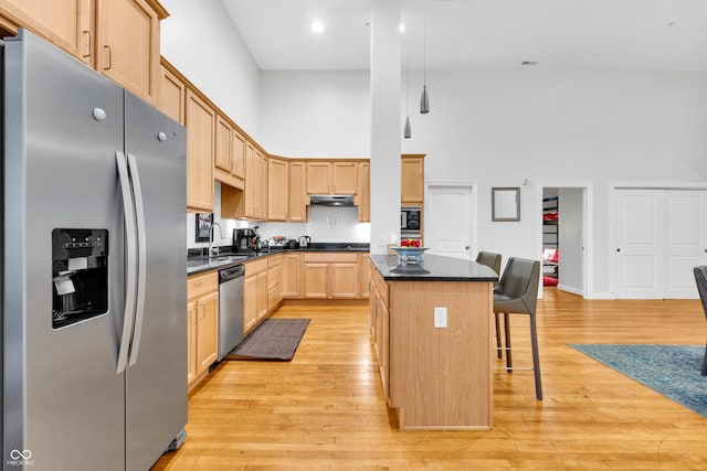 kitchen with a center island, a towering ceiling, a breakfast bar area, light brown cabinetry, and appliances with stainless steel finishes