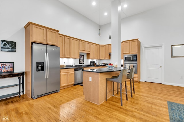 kitchen featuring a kitchen breakfast bar, stainless steel appliances, light hardwood / wood-style flooring, a high ceiling, and a center island