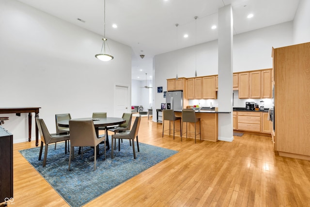 dining room with ceiling fan, light hardwood / wood-style floors, and a high ceiling