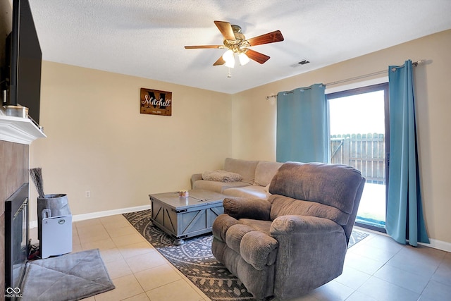 living room featuring a tiled fireplace, ceiling fan, light tile patterned flooring, and a textured ceiling